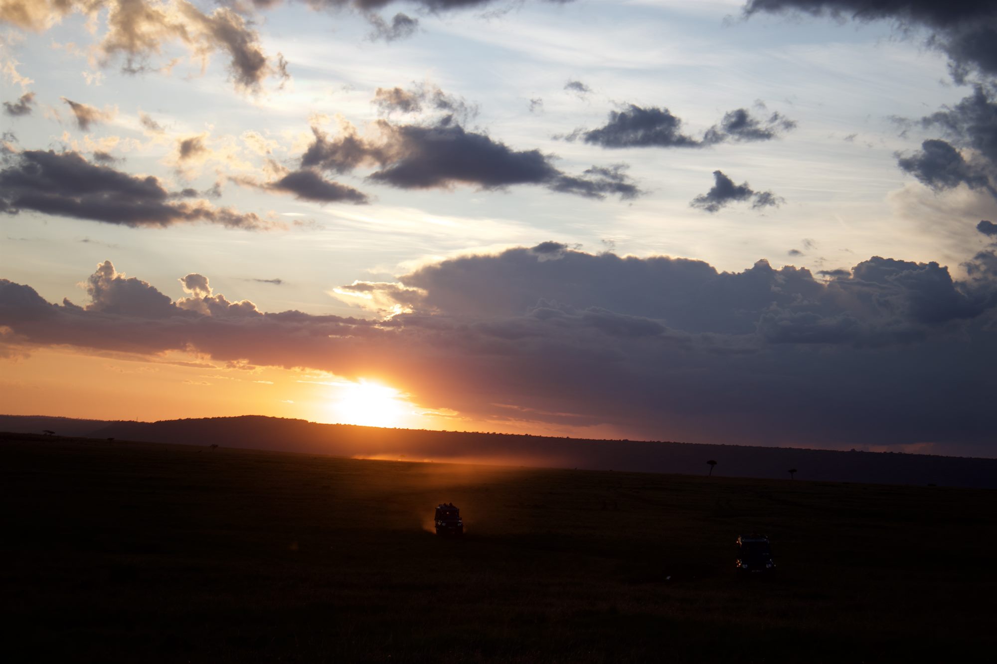 Sun setting over the Kenyan plains with vehicles on the track